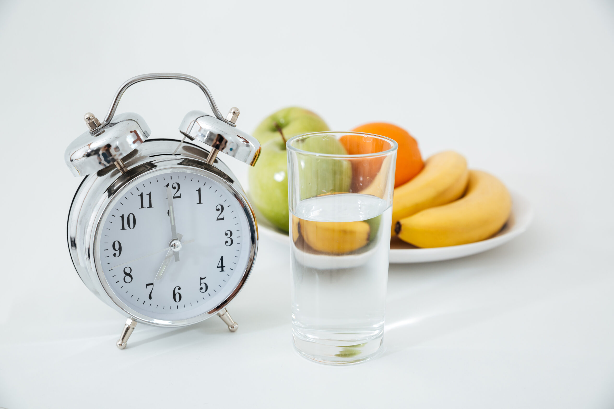 Image of alarm and glass of water near fruits over white background